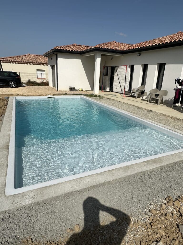 Piscine rectangulaire moderne et maison contemporaine Piscine rectangulaire moderne devant une maison blanche neuve avec toit en tuiles rouges et jardin en gravier.
